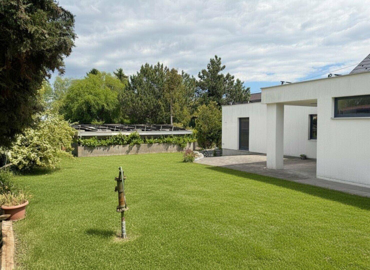 Weitläufiger Garten mit gepflegtem Rasen, alter Wasserpumpe und Blick auf das Haus.