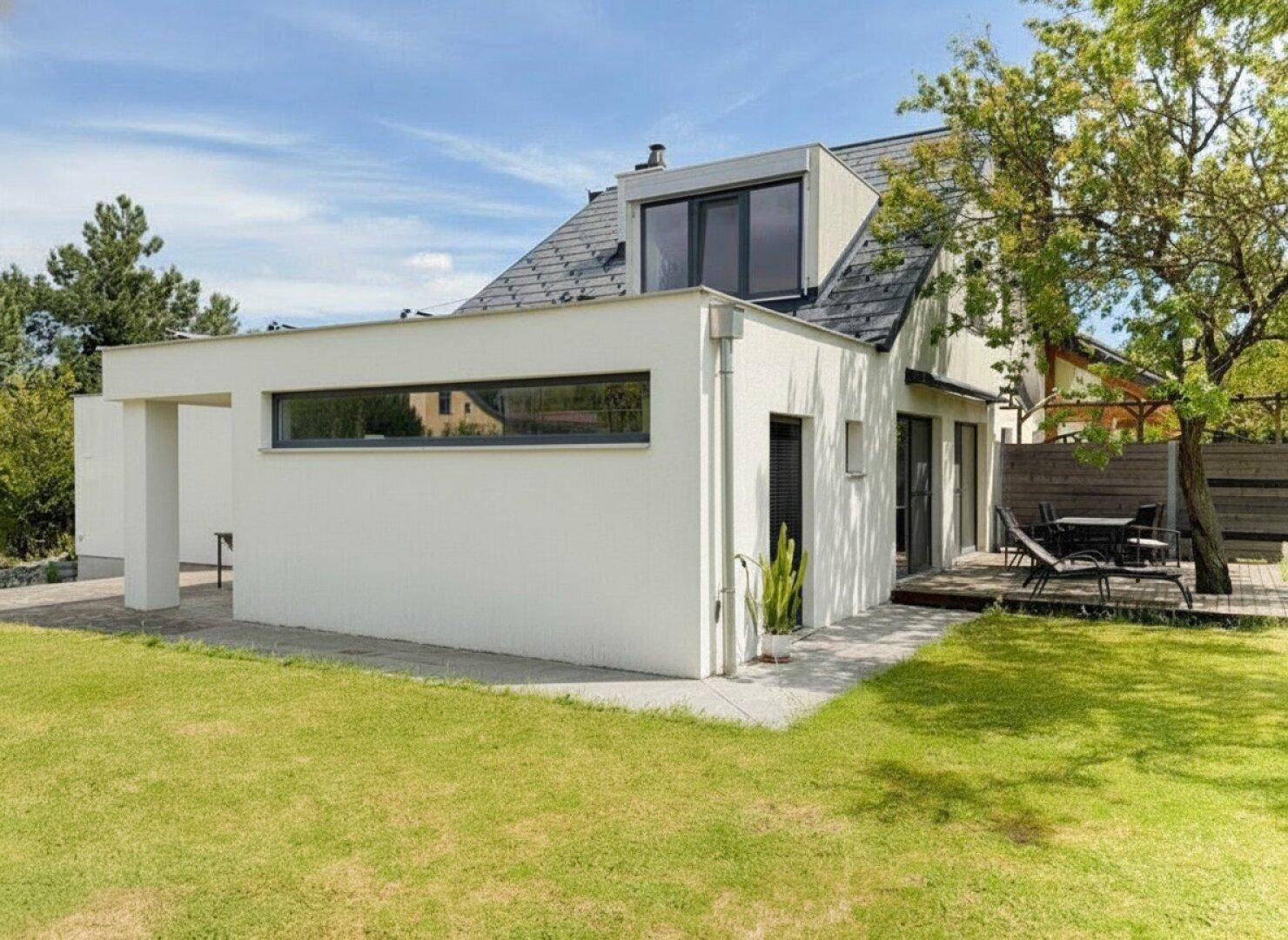 Rückseite des Hauses mit Holzterrasse, Gartenmöbeln und angrenzender Rasenfläche.