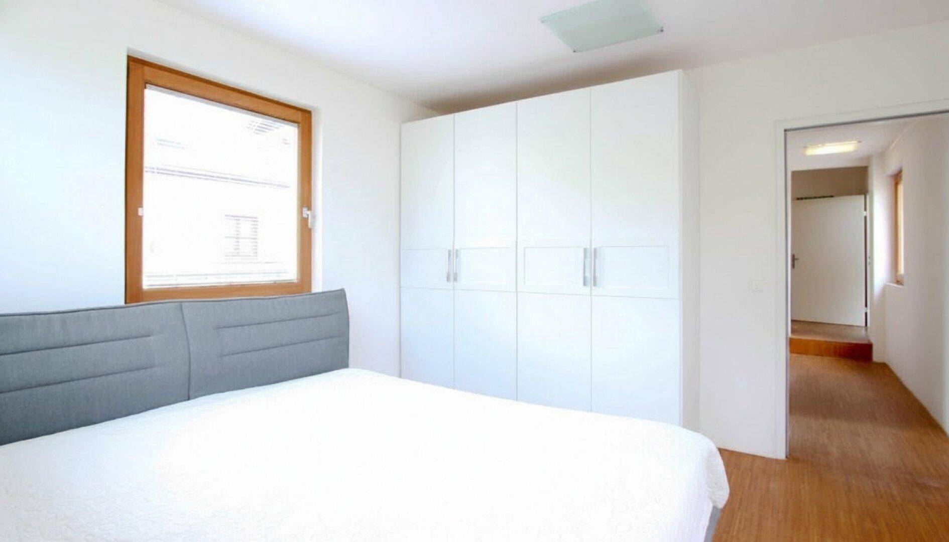 Helles Schlafzimmer mit großem Bett, weißen Einbauschränken und Holzboden.