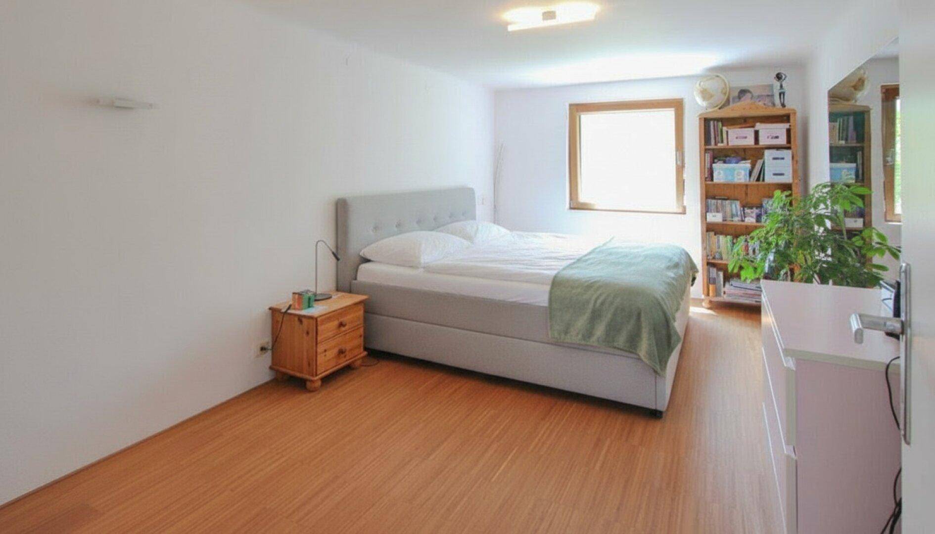 Geräumiges Schlafzimmer mit Doppelbett, Bücherregal und Blick ins Grüne.
