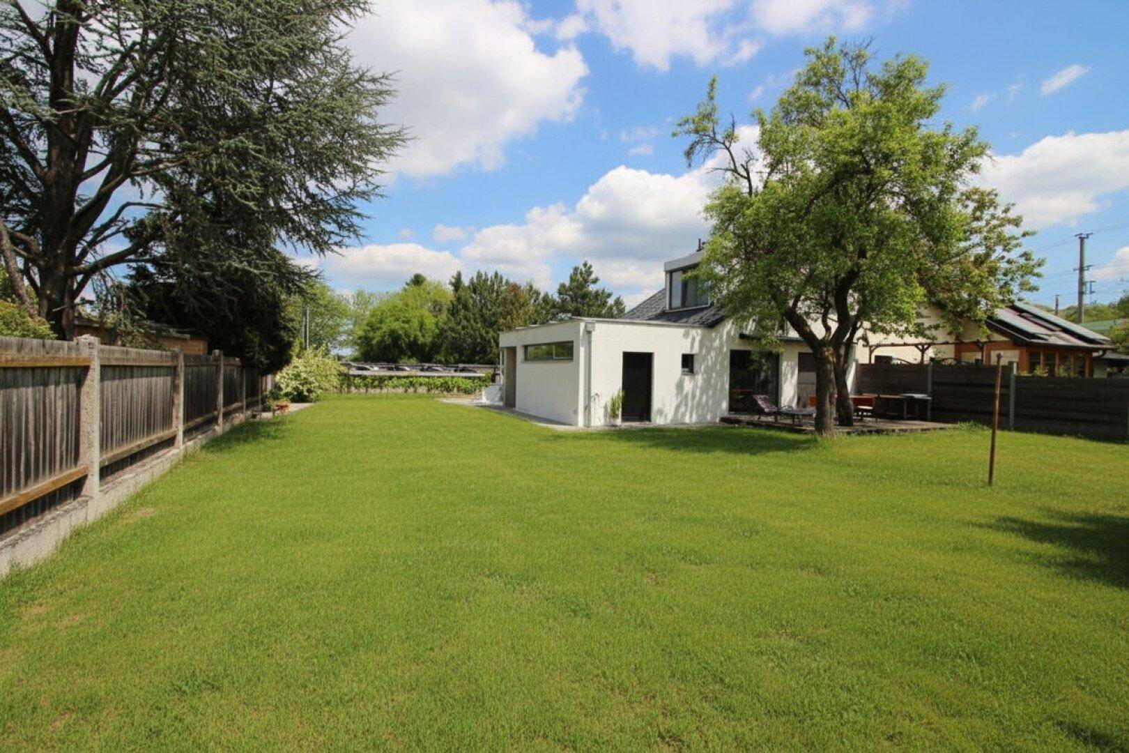 Weitläufiger Garten mit gepflegtem Rasen und moderner Hausfassade unter blauem Himmel.
