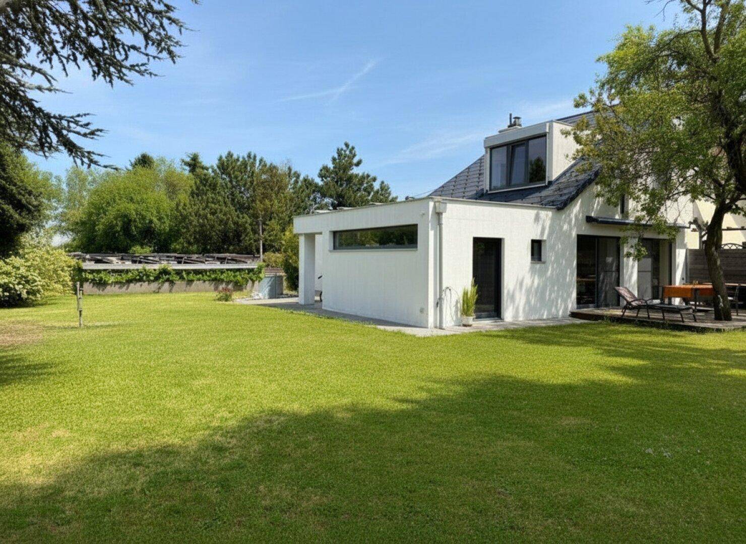 Seitenansicht des Hauses mit weitläufigem Rasen und altem Baumbestand.