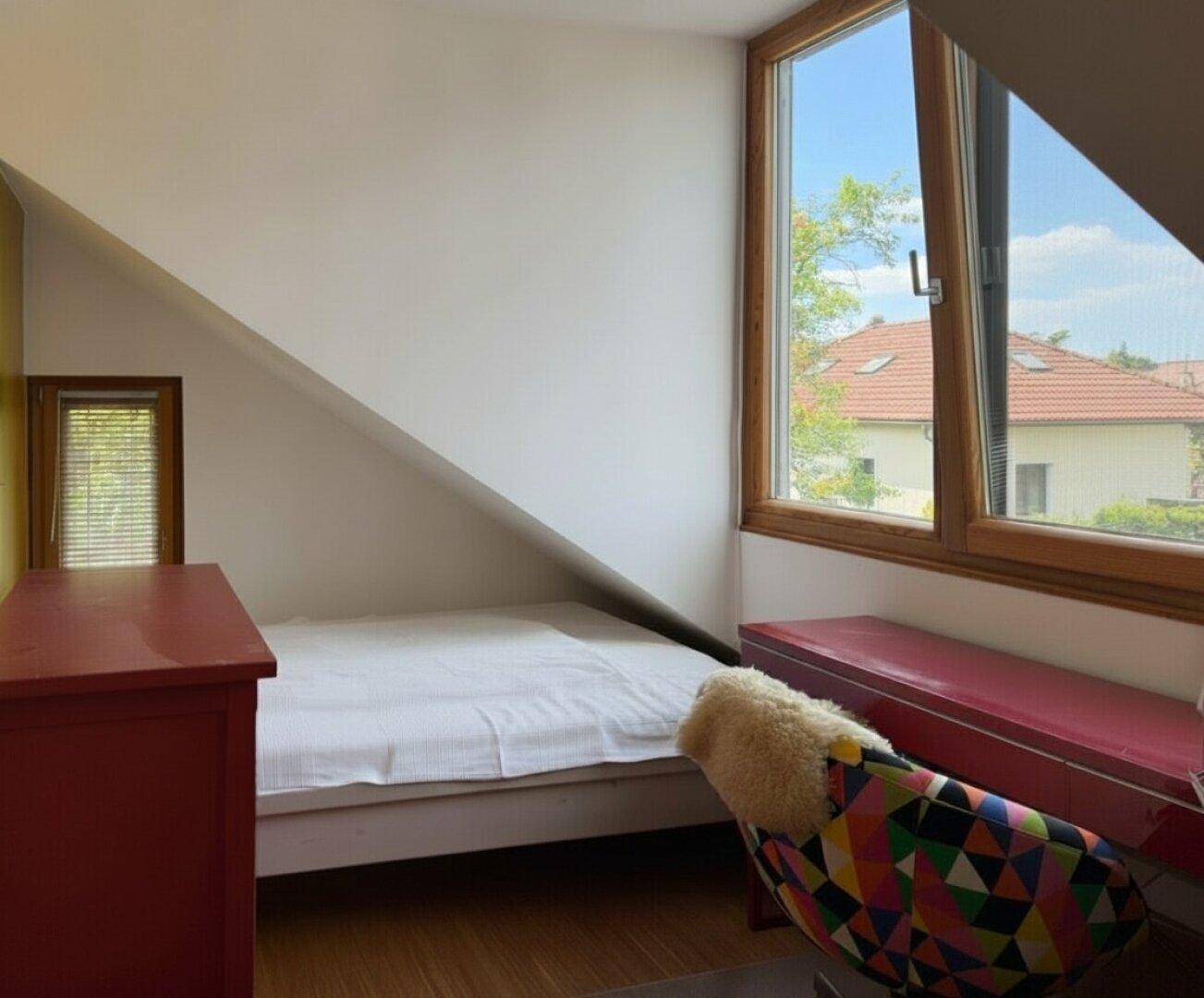 Gemütliches Schlafzimmer im Dachgeschoss mit schrägen Wänden und großem Fenster.