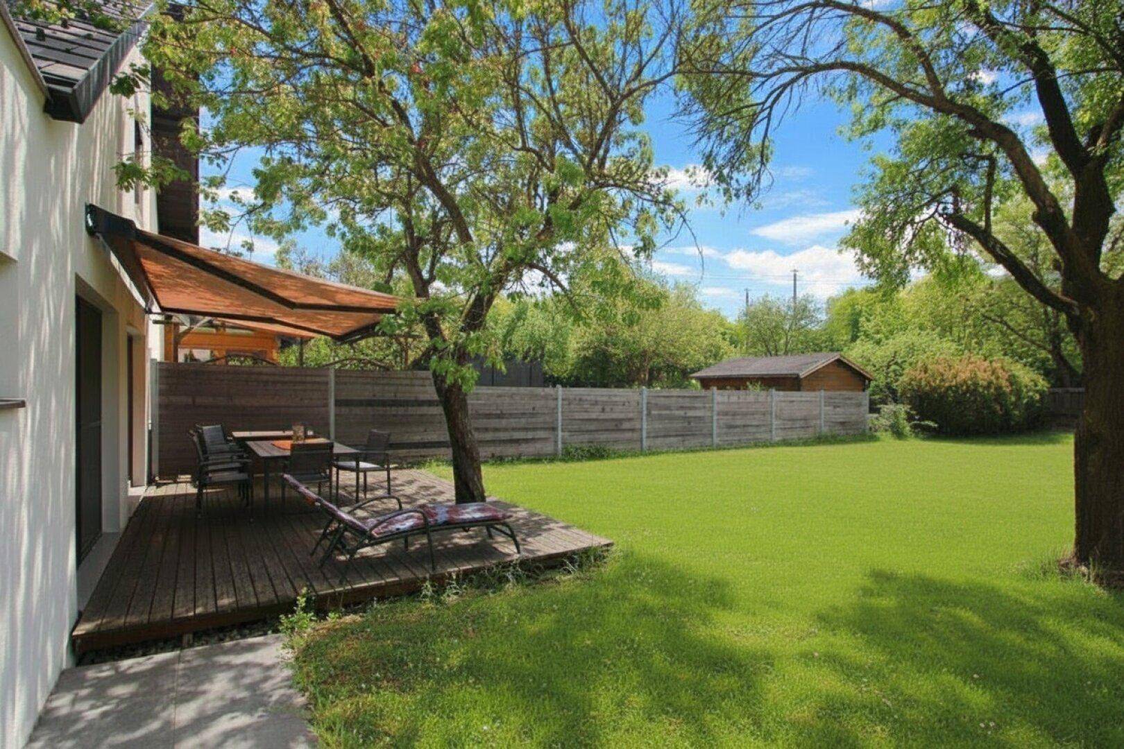 Gemütliche Holzterrasse mit Sonnenschutz, Essbereich und weitem Blick in den Garten.