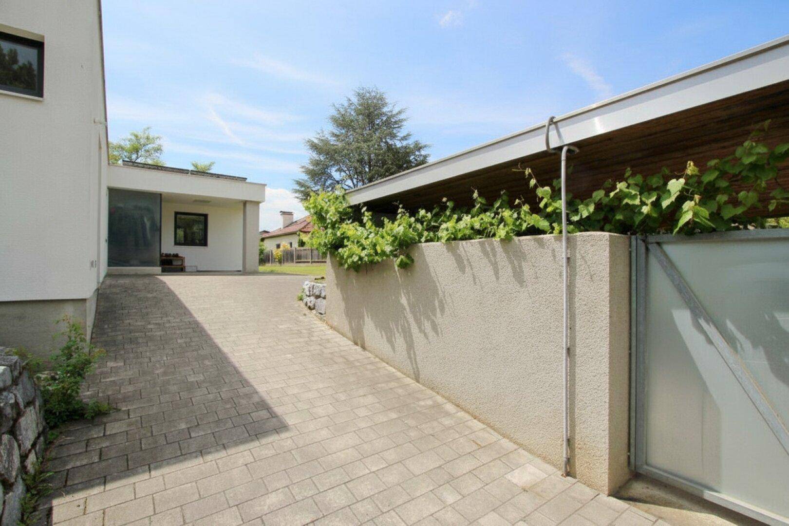 Gepflasterte Zufahrt zum Hauseingang mit moderner Architektur und begrünten Mauern.