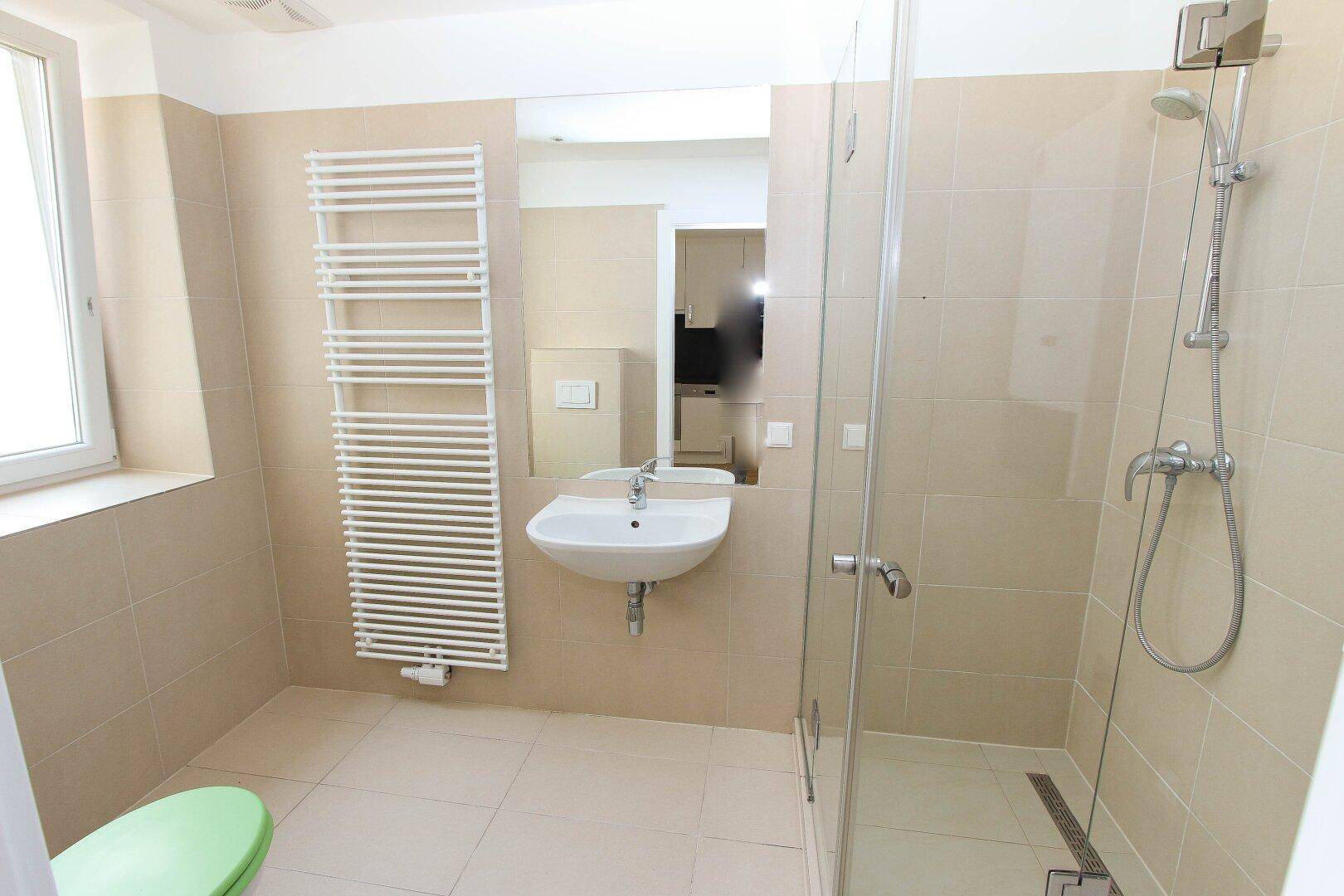 Modernes Badezimmer mit beigen Fliesen, Duschkabine, Waschbecken und Handtuchheizkörper.