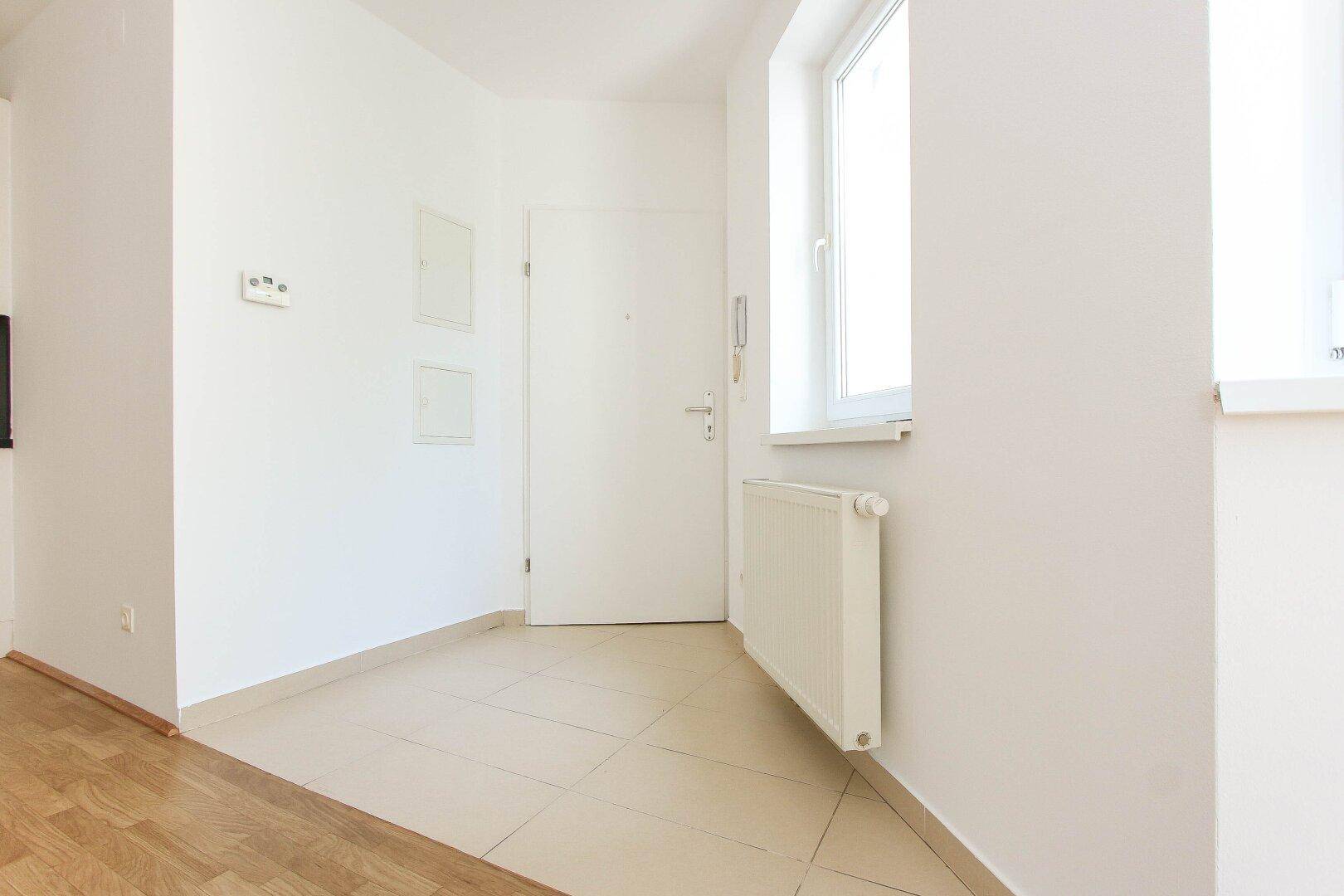 Heller Eingangsbereich mit Fliesenboden, weißer Eingangstür und Gegensprechanlage.