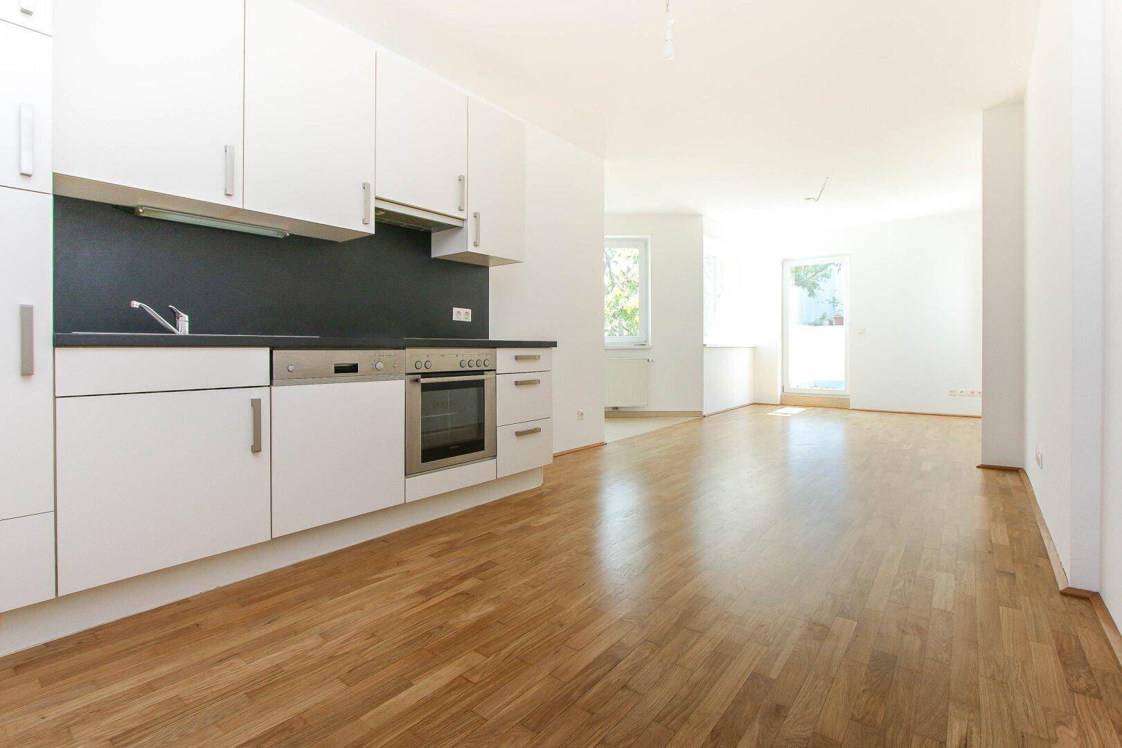 Offener Wohnbereich mit integrierter Küche, Holzboden und viel Tageslicht durch große Fenster.