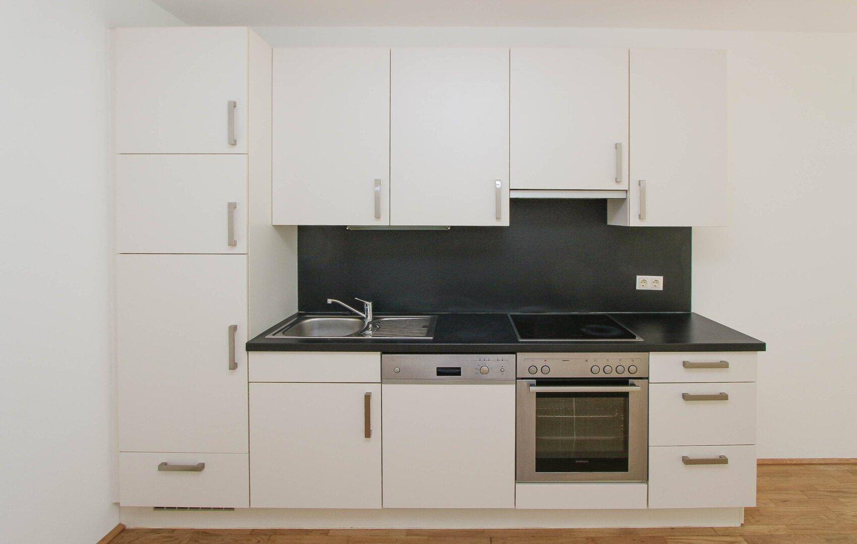 Moderne Einbauküche mit weißen Schränken, dunkler Arbeitsplatte und Edelstahlgeräten.