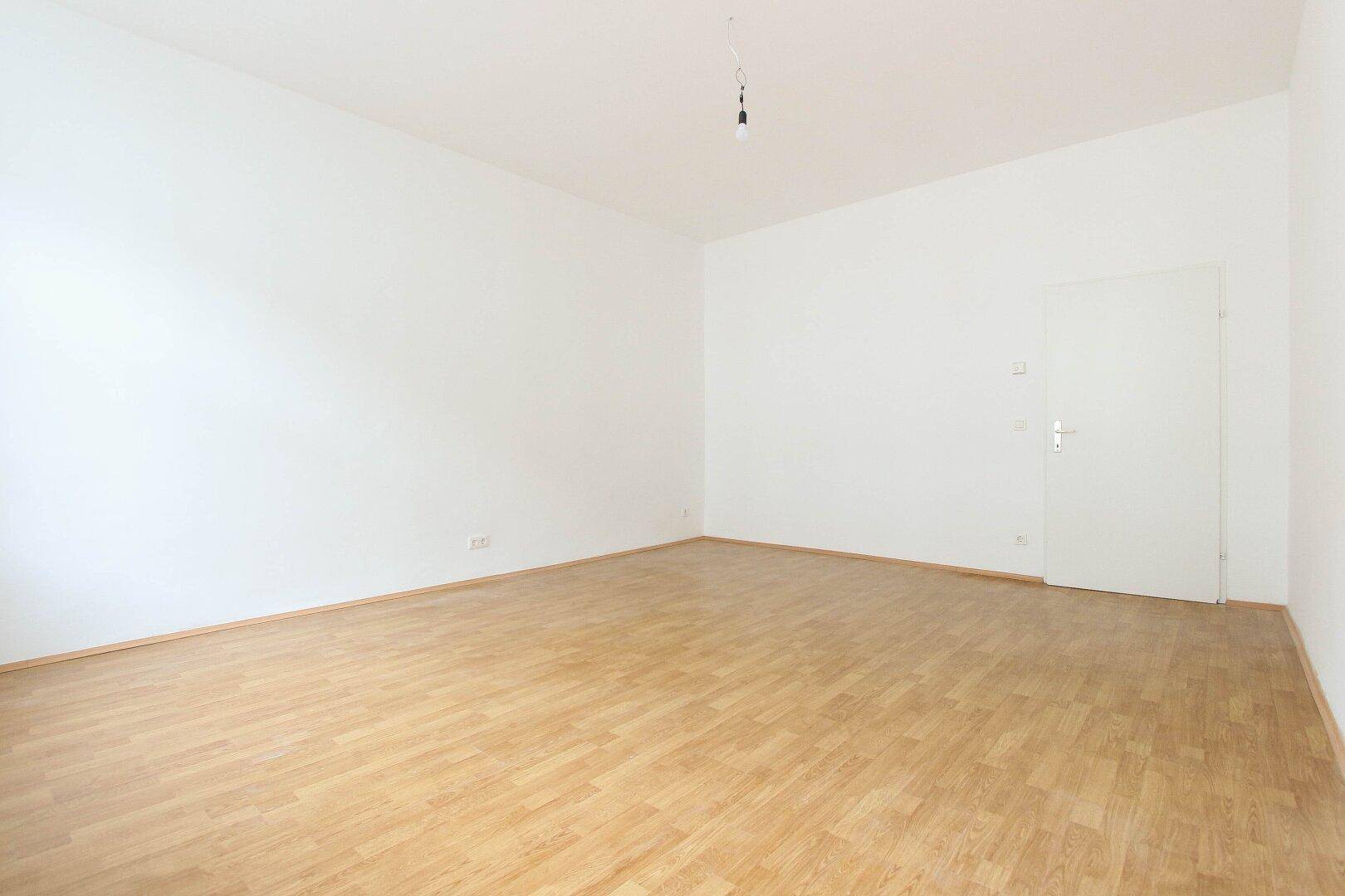 Geräumiges, helles Zimmer mit Parkettboden und weißer Tür, ideal für vielfältige Nutzung.
