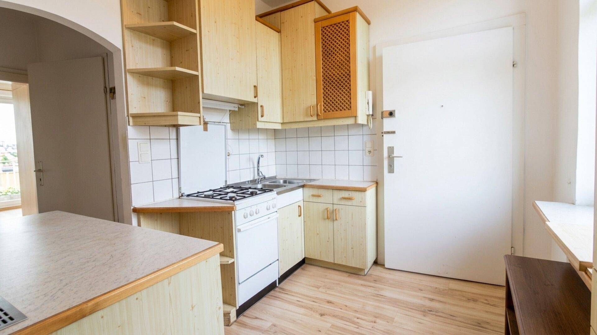 Einfache Küche mit Holzfronten, Gasherd und Blick auf einen angrenzenden Raum.
