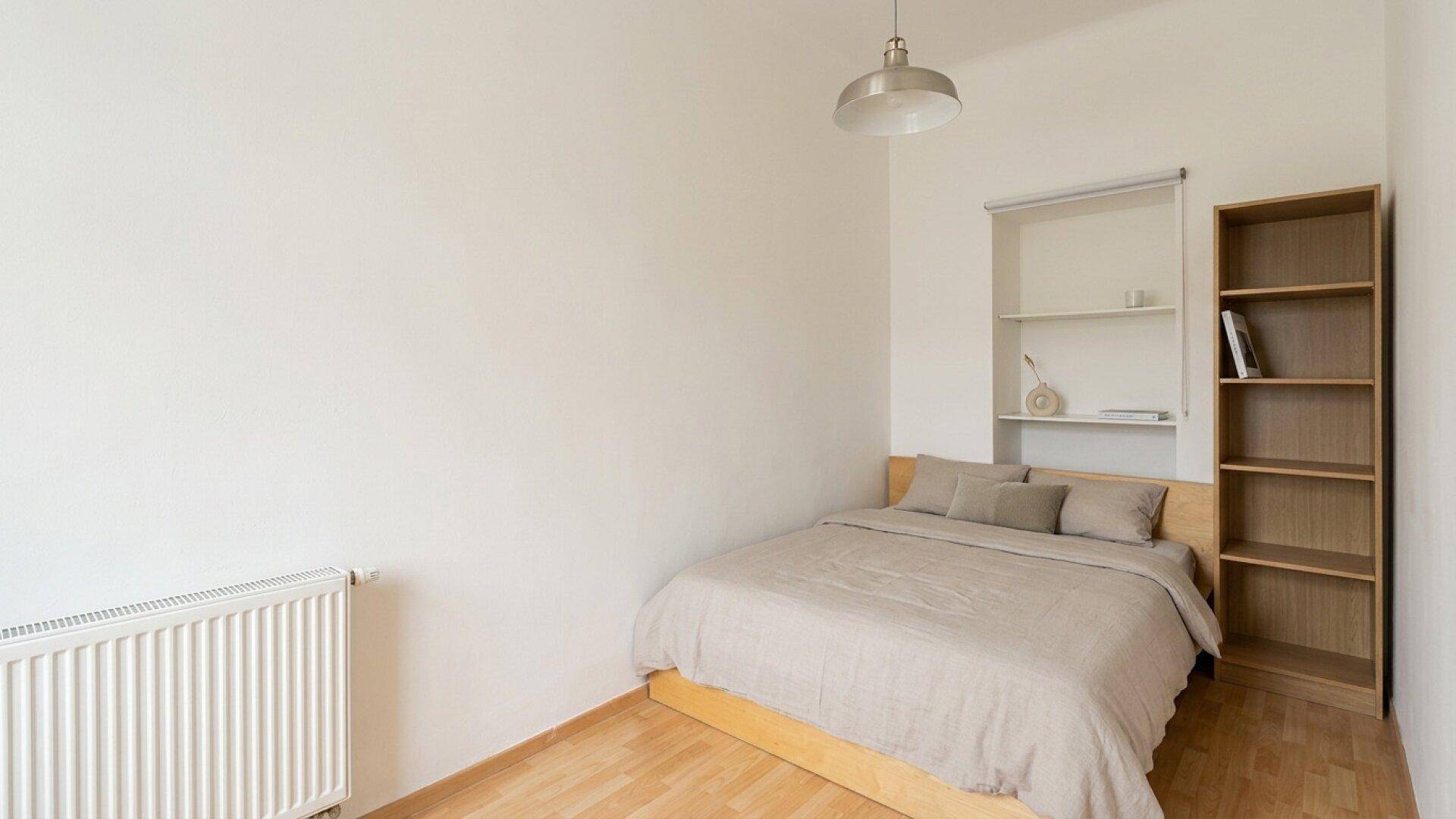 Gemütliches Schlafzimmer mit Bett, Regal und Laminatboden, ideal für eine Person.