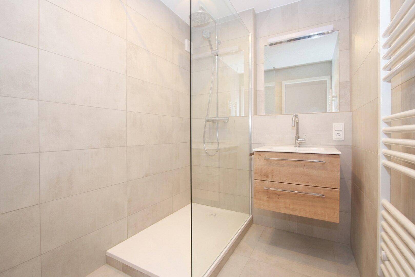 Zeitgemäßes Badezimmer mit großer begehbarer Dusche, schwebendem Waschtisch und beheiztem Handtuchhalter.