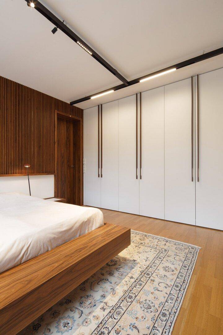 Schlafzimmer mit Holzbett, Einbauschränken und moderner Wandverkleidung.