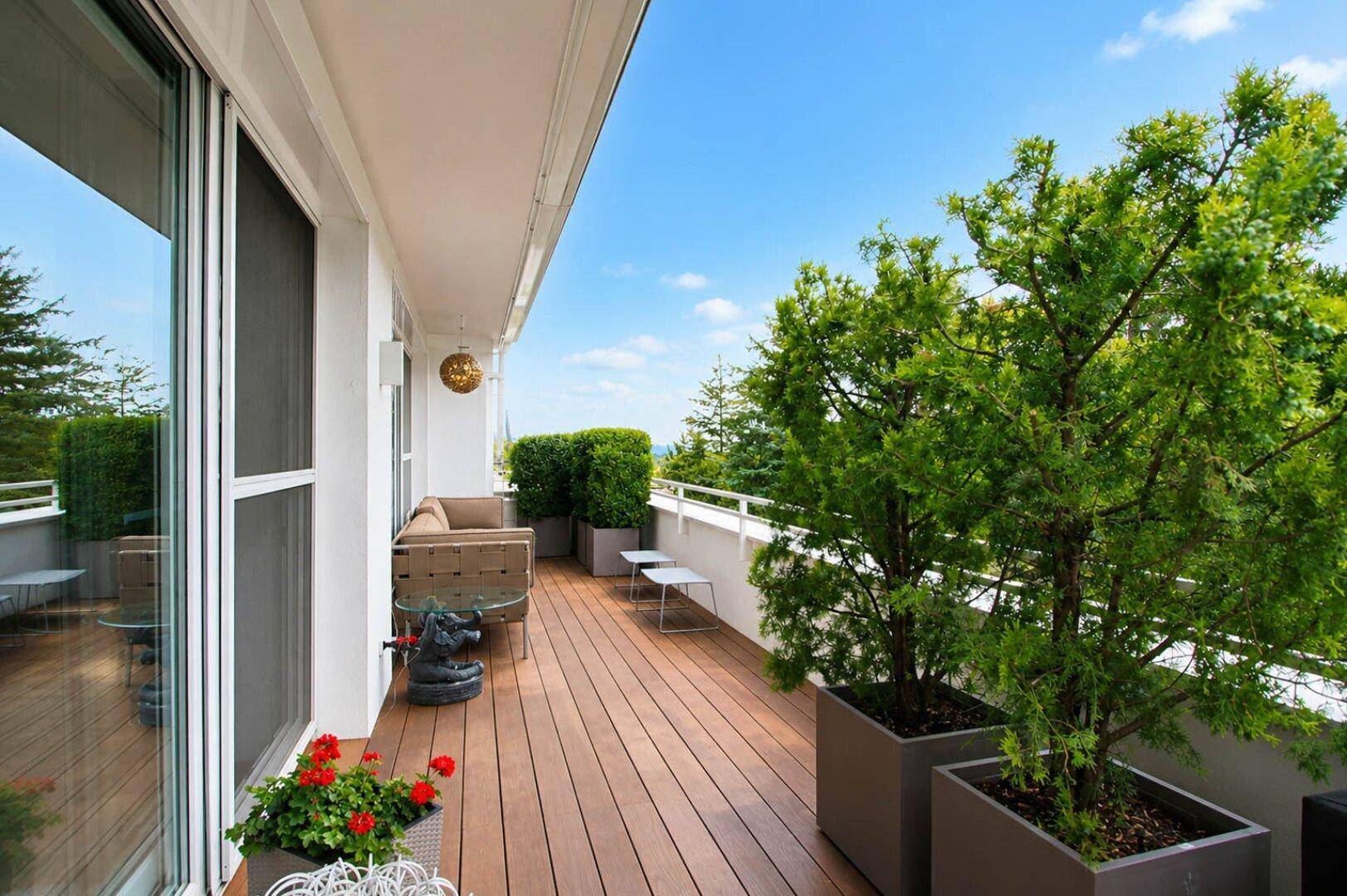 Geräumige Holzterrasse mit Pflanzen und Sitzgelegenheiten unter blauem Himmel.