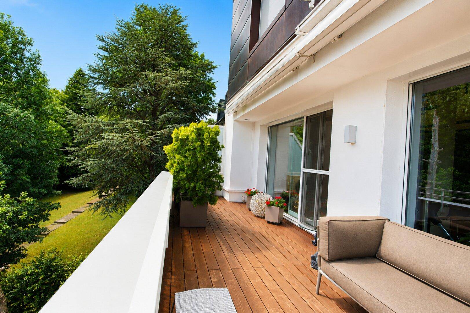 Breite Terrasse mit Holzboden, Pflanzen und weitem Blick in den Garten.