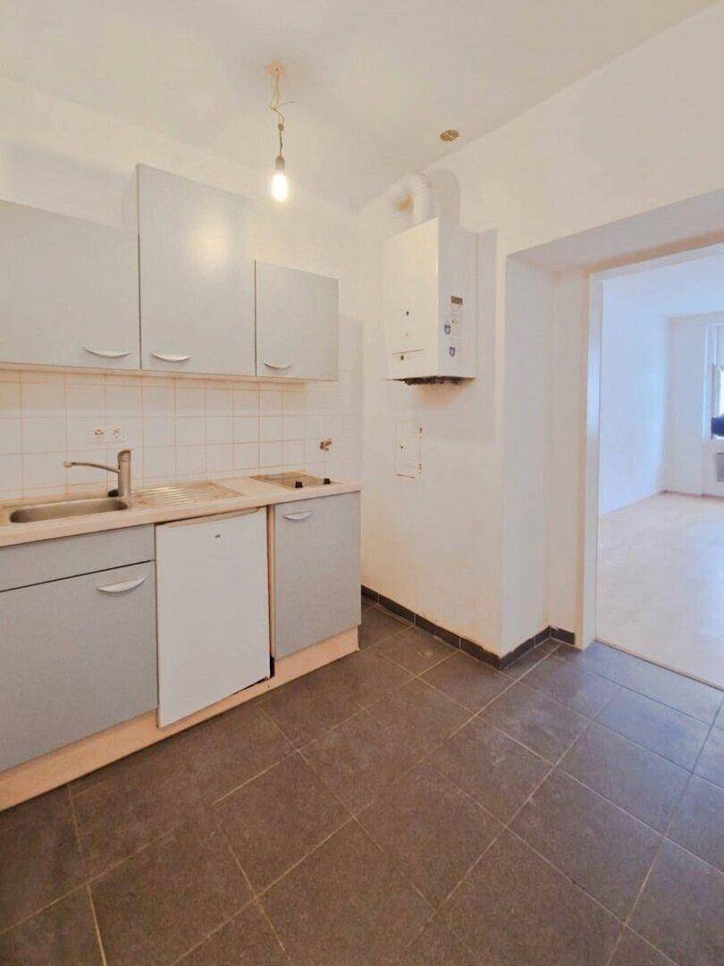 Funktionale Küche mit grauen Unterschränken, Spüle und einem an der Wand montierten Heizkessel.