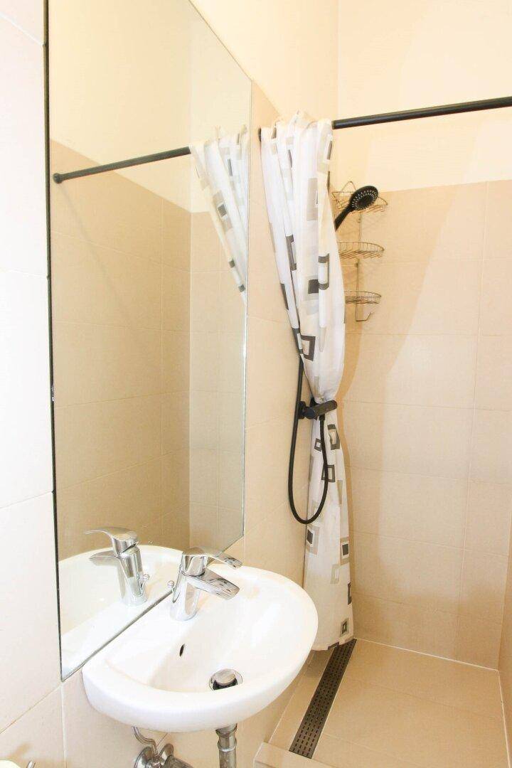 Badezimmer mit Duschbereich, Waschbecken und großem Spiegel, ausgestattet mit beigefarbenen Fliesen.