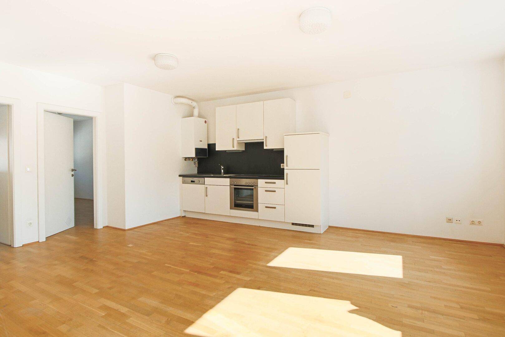 Geräumiger Wohnbereich mit integrierter Küchenzeile, Parkettboden und viel Tageslicht.