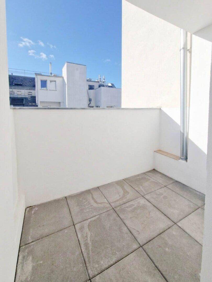 Kleiner Balkon mit Fliesenboden und Blick auf umliegende Gebäude.