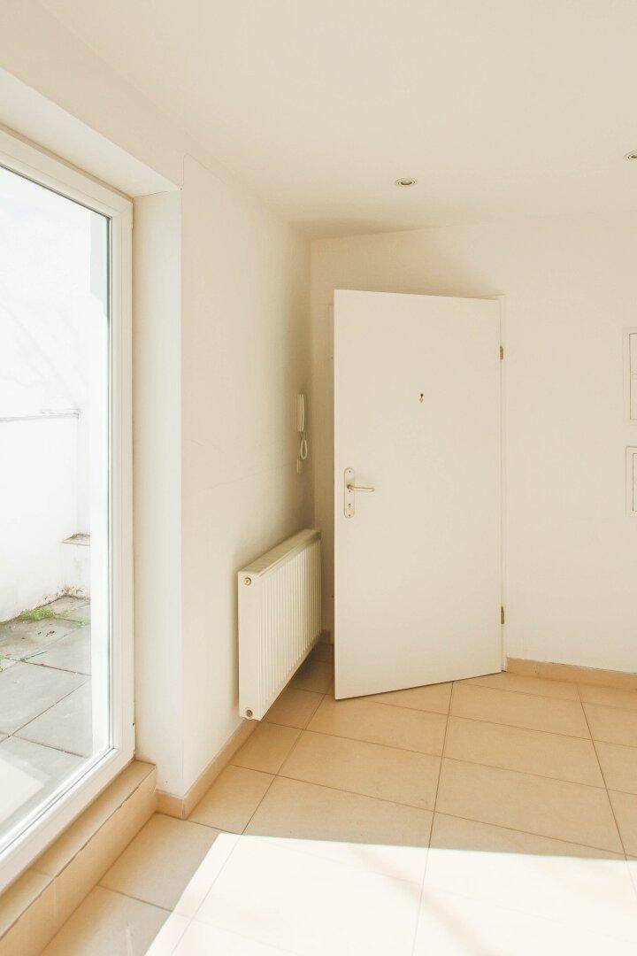 Heller Eingangsbereich mit Fliesenboden, großer Tür und Zugang zu einem Außenbereich.