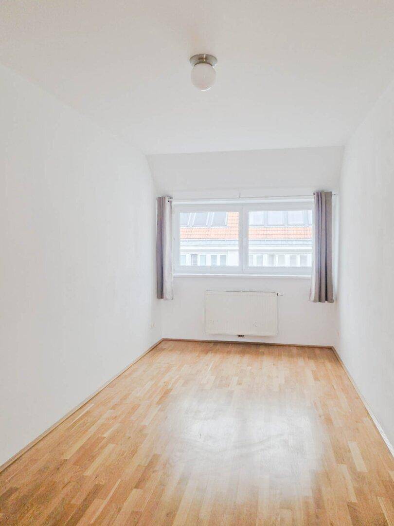 Gemütliches Zimmer mit Parkettboden und einem großen Fenster, ideal als Schlafzimmer.