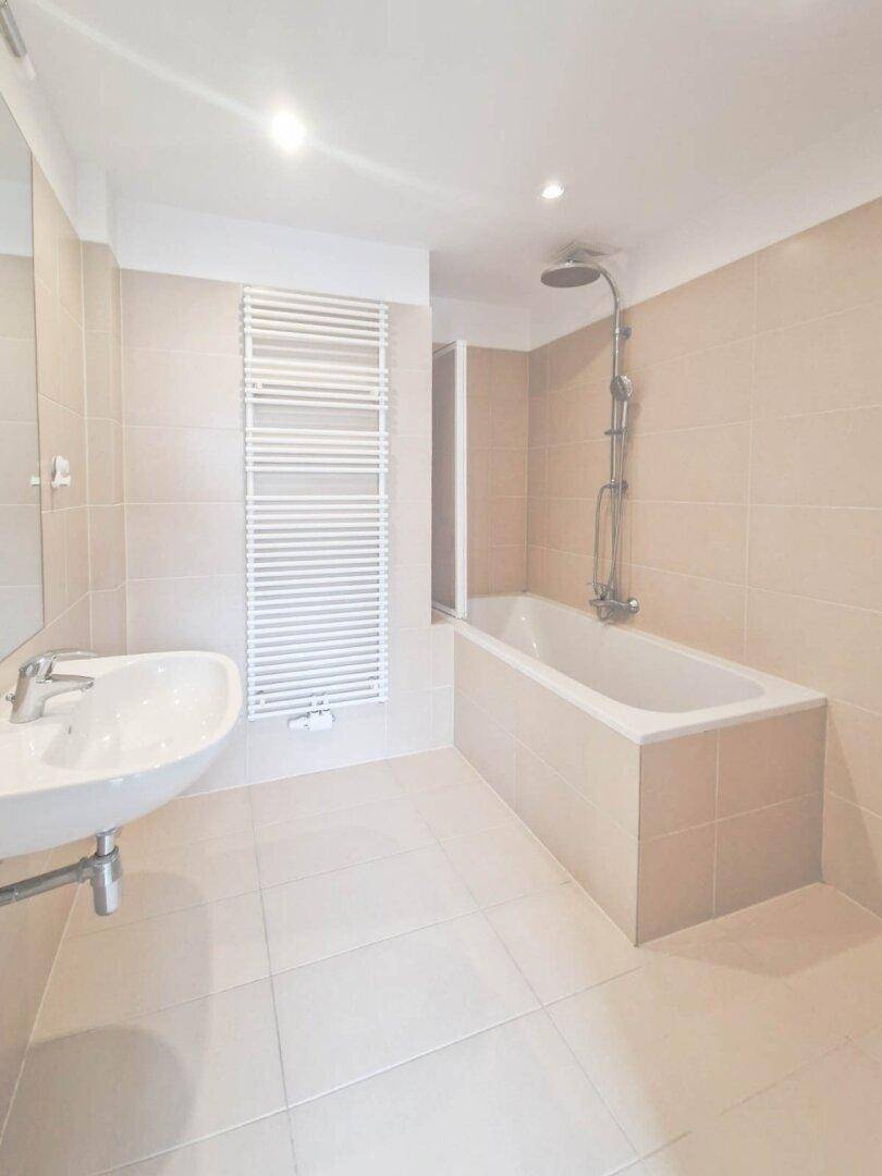Modernes Badezimmer mit beigefarbenen Fliesen, Badewanne, Dusche und Handtuchheizkörper.