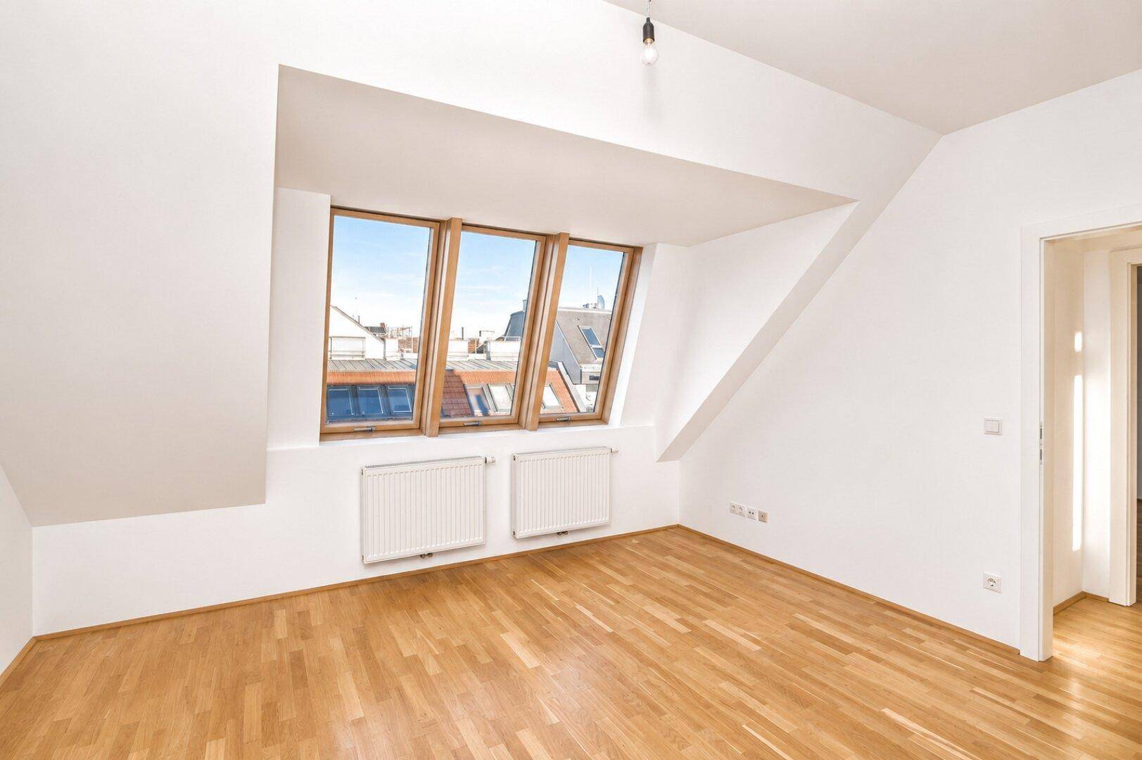 Geräumiges Dachzimmer mit Parkettboden, schrägen Wänden und mehreren Dachfenstern.