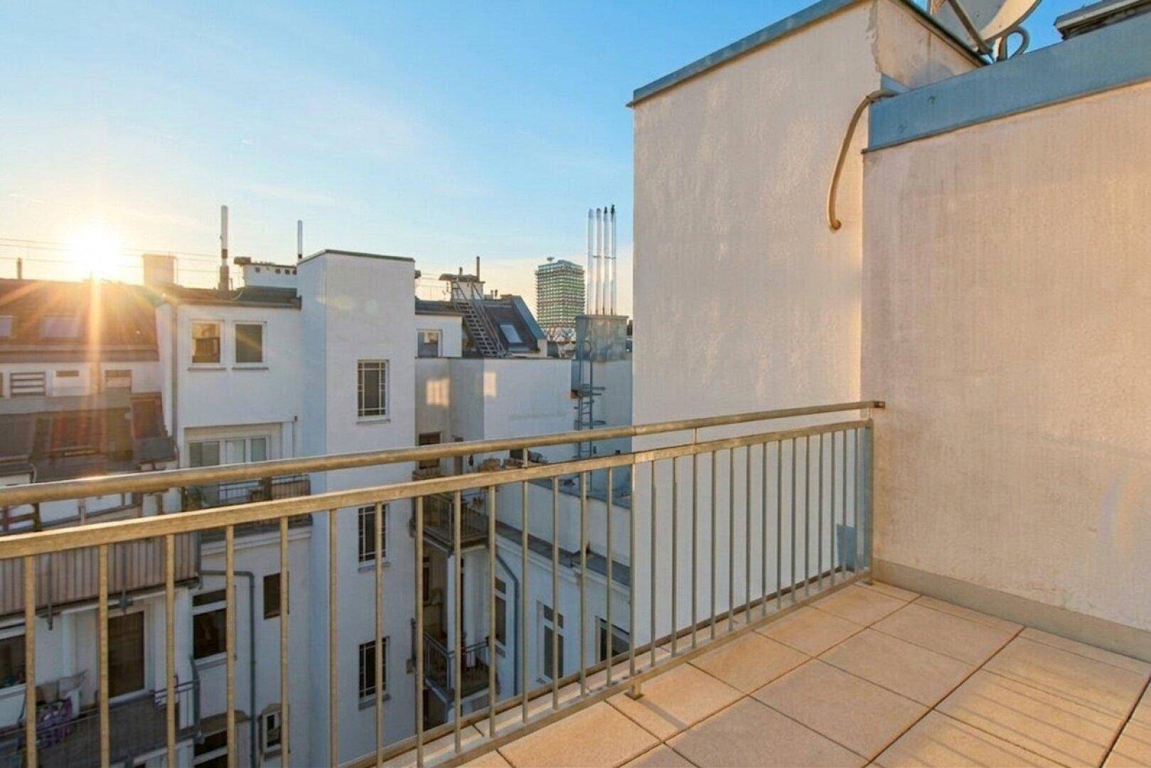 Sonniger Balkon mit weitem Blick über die Dächer der Stadt bei Sonnenuntergang.