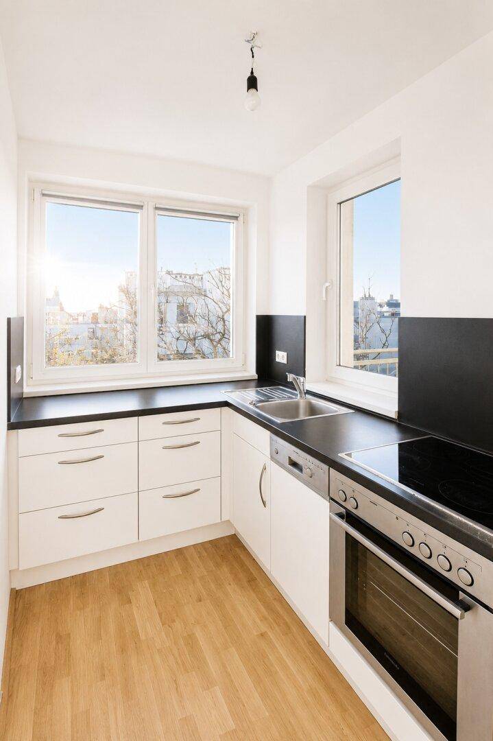 Moderne Einbauküche mit weißen Schränken, schwarzen Arbeitsplatten und integrierten Geräten.