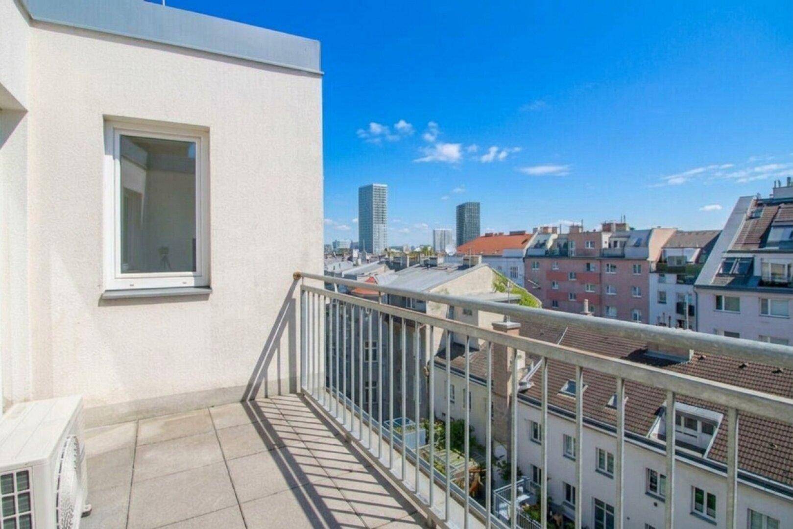Balkon mit Stadtblick und moderner Architektur im Hintergrund unter blauem Himmel.