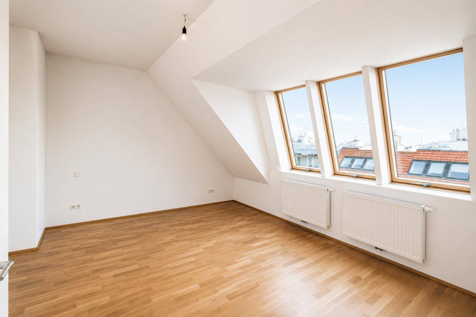 Großer Dachgeschossraum mit Parkettboden, schrägen Wänden und hellen Dachfenstern.