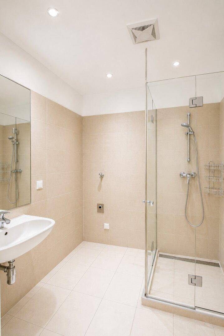 Modernes Badezimmer mit begehbarer Glasdusche, Waschbecken und hellen Fliesen.