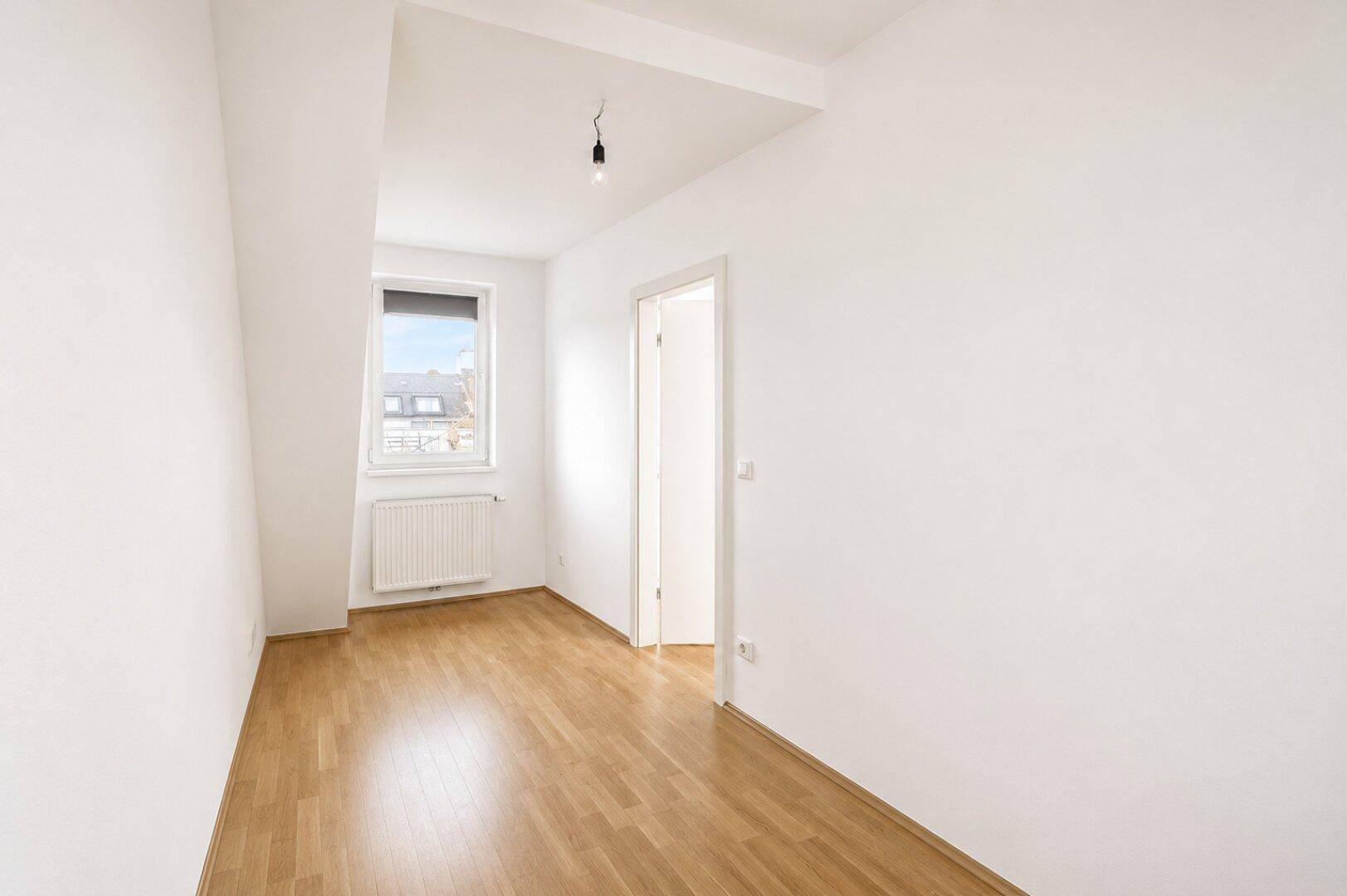 Heller, leerer Raum mit Parkettboden und einem Fenster, ideal als Schlafzimmer.