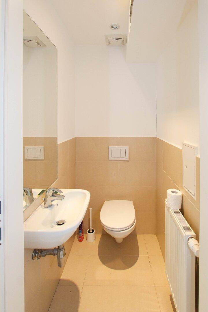 Kleines Gäste-WC mit Wand-WC, Waschbecken und beigefarbenen Fliesen an den Wänden.