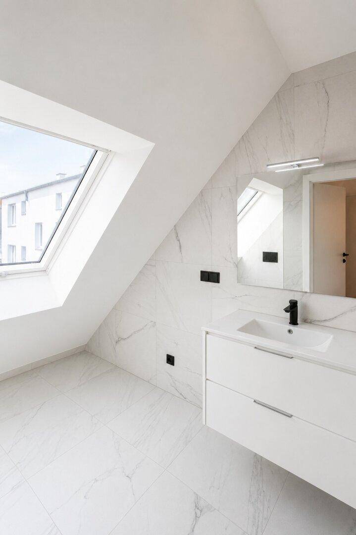 Modernes Badezimmer mit Marmorfliesen, schwebendem Waschtisch und großem Dachfenster für viel Licht.