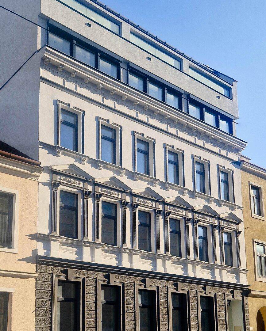 Historische Fassade eines Gebäudes mit modernen Erweiterungen im oberen Bereich.