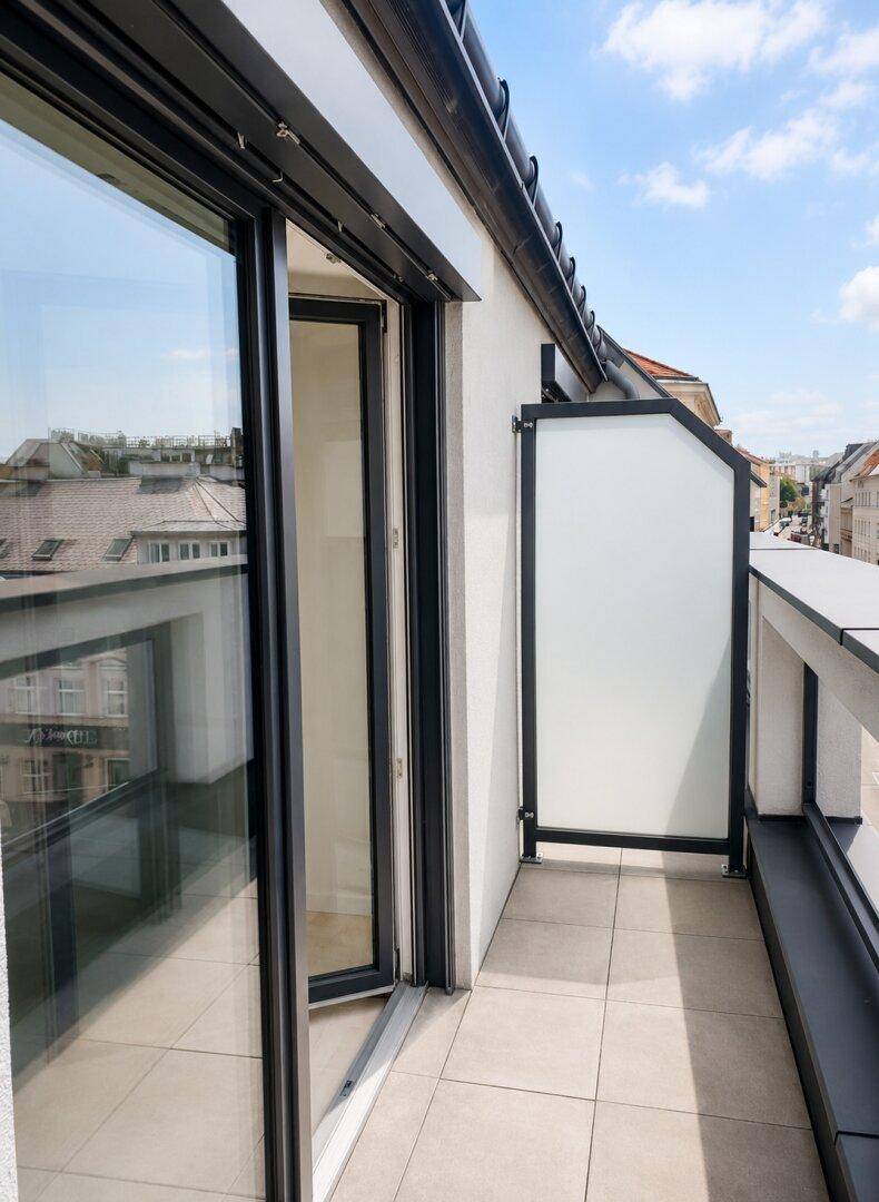 Kleiner Balkon mit Fliesenboden und Blick auf die umliegenden Dächer der Stadt.