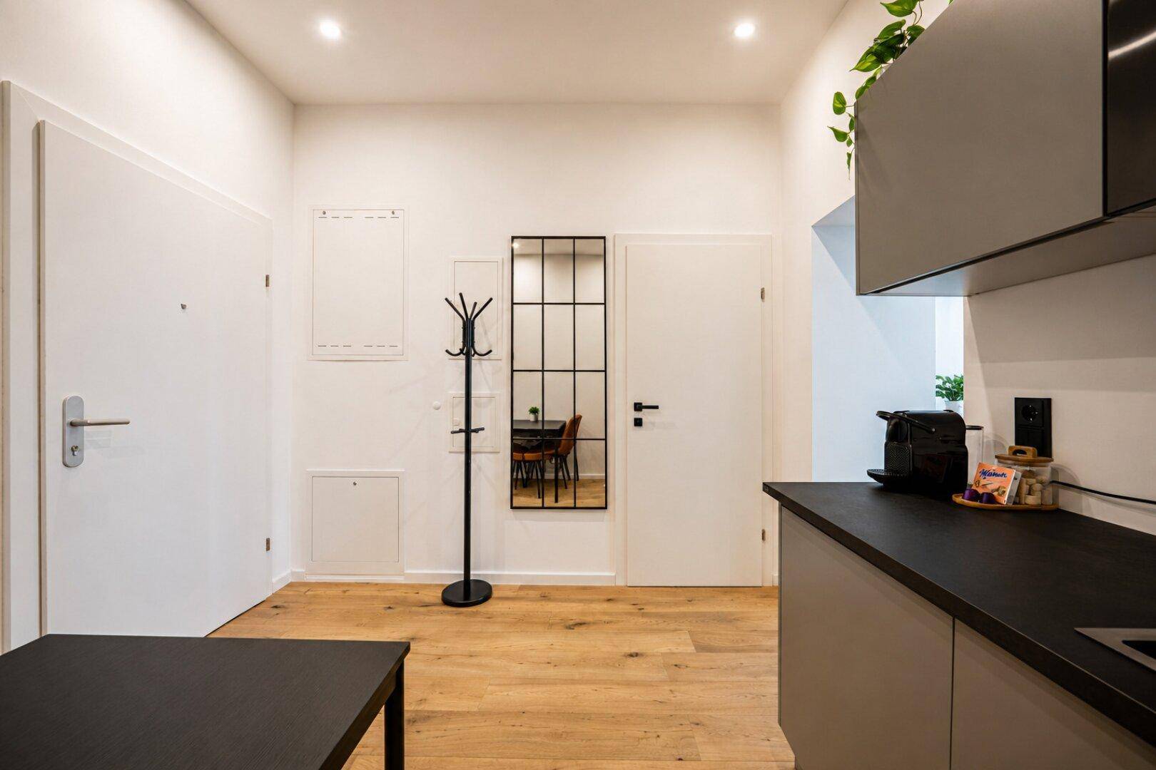 Heller Eingangsbereich mit Garderobe, großem Spiegel und Zugang zur Küchenzeile.