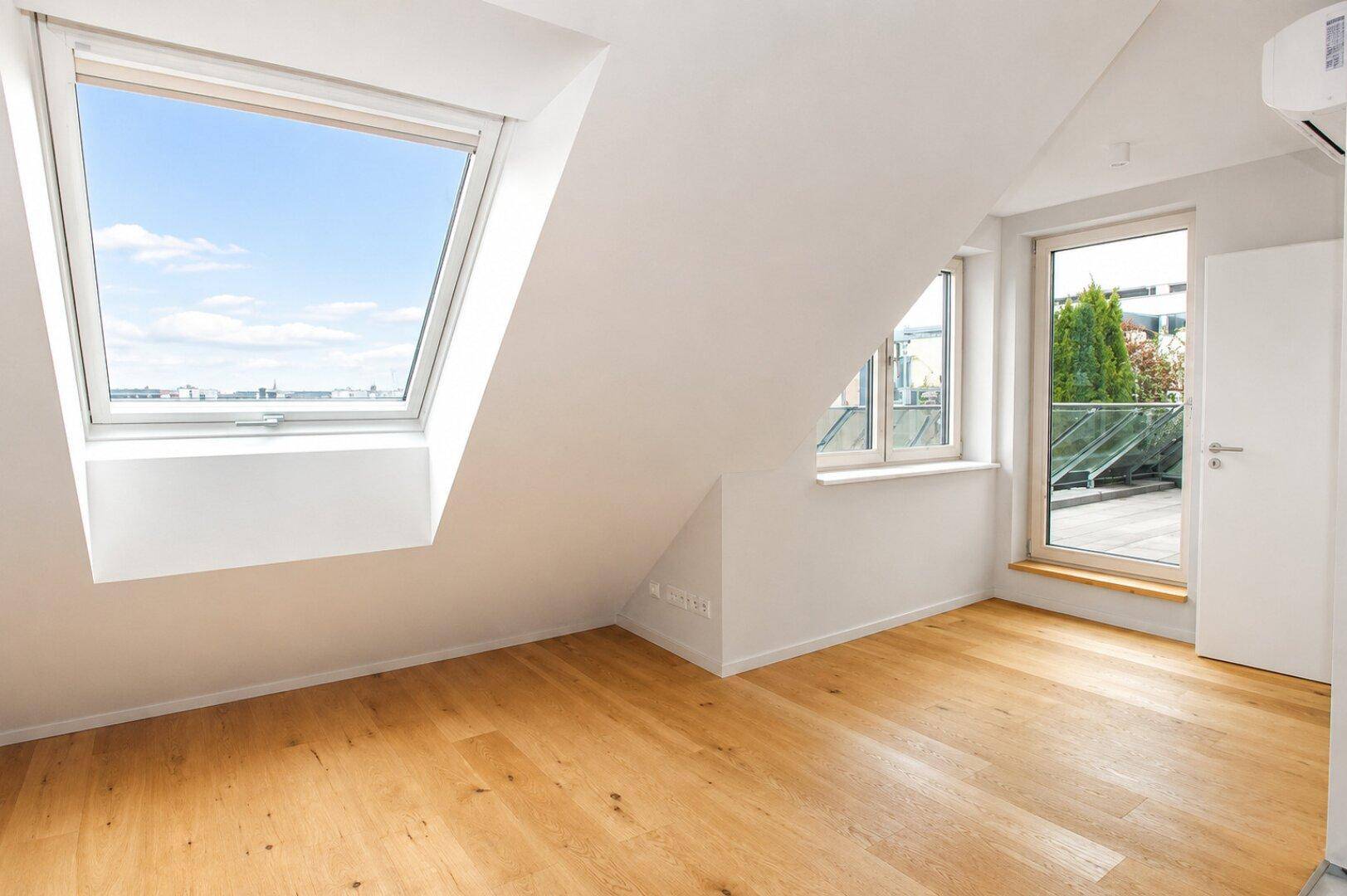 Helles Zimmer mit Holzboden, Dachfenster und Zugang zur Terrasse.