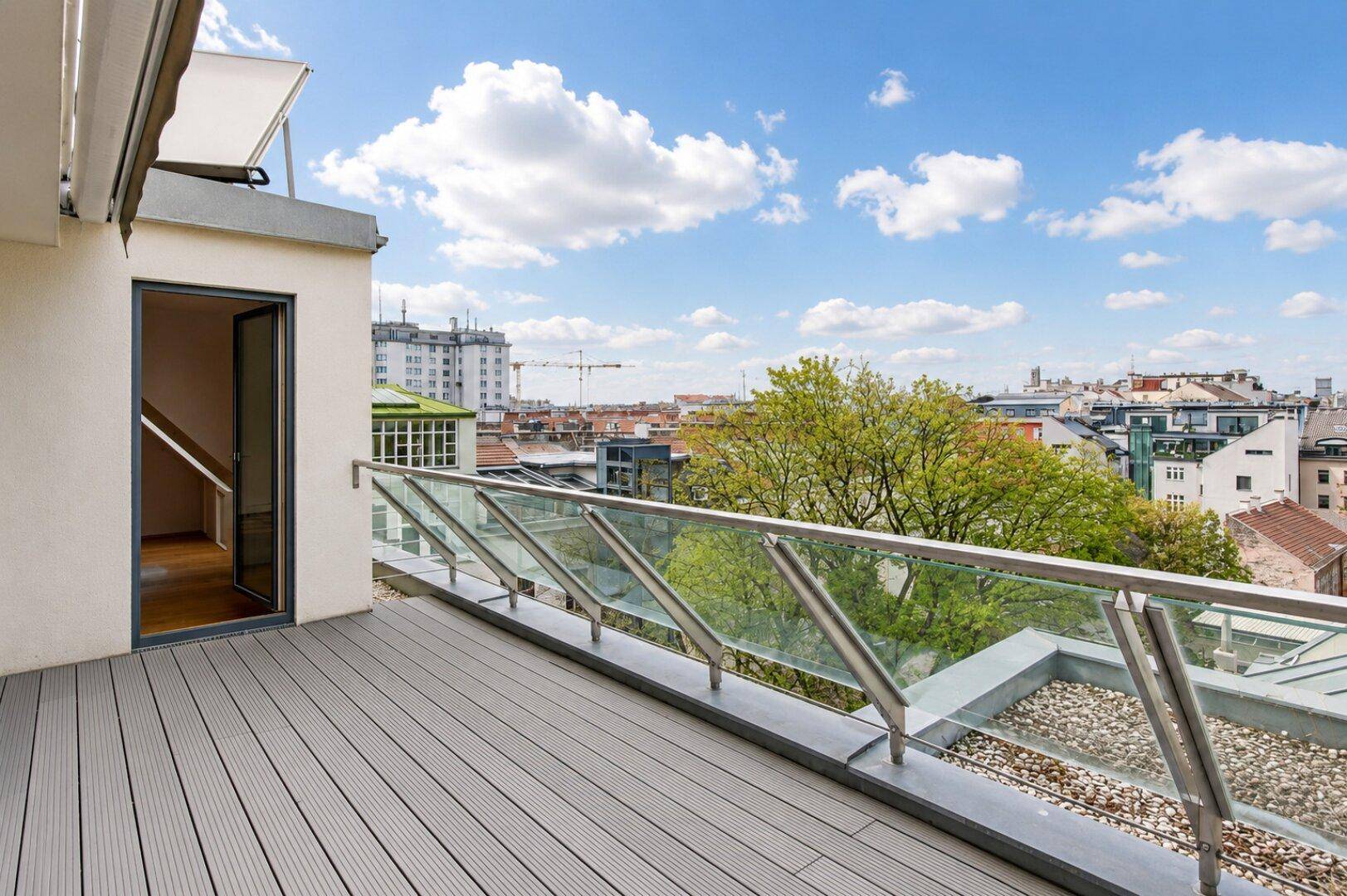 Geräumige Dachterrasse mit Holzdielenboden, Glasgeländer und weitem Stadtblick.