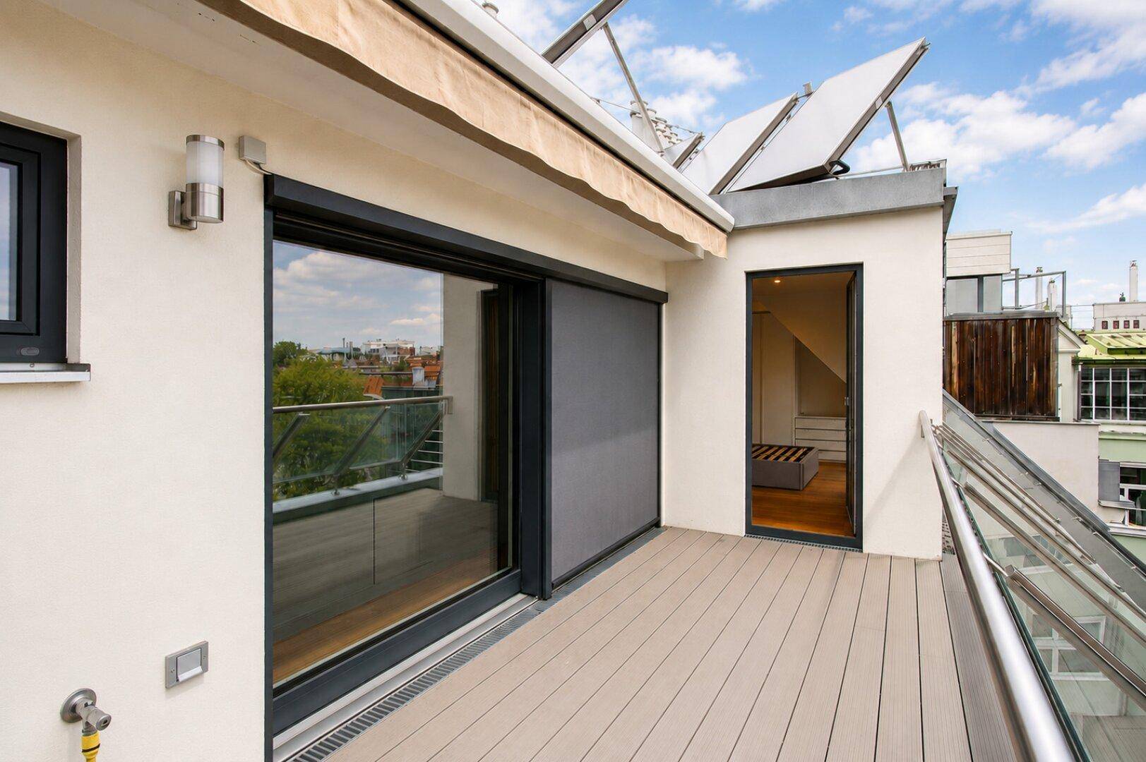 Dachterrasse mit Schiebetüren, Markise und Solarpaneelen auf dem Dach.