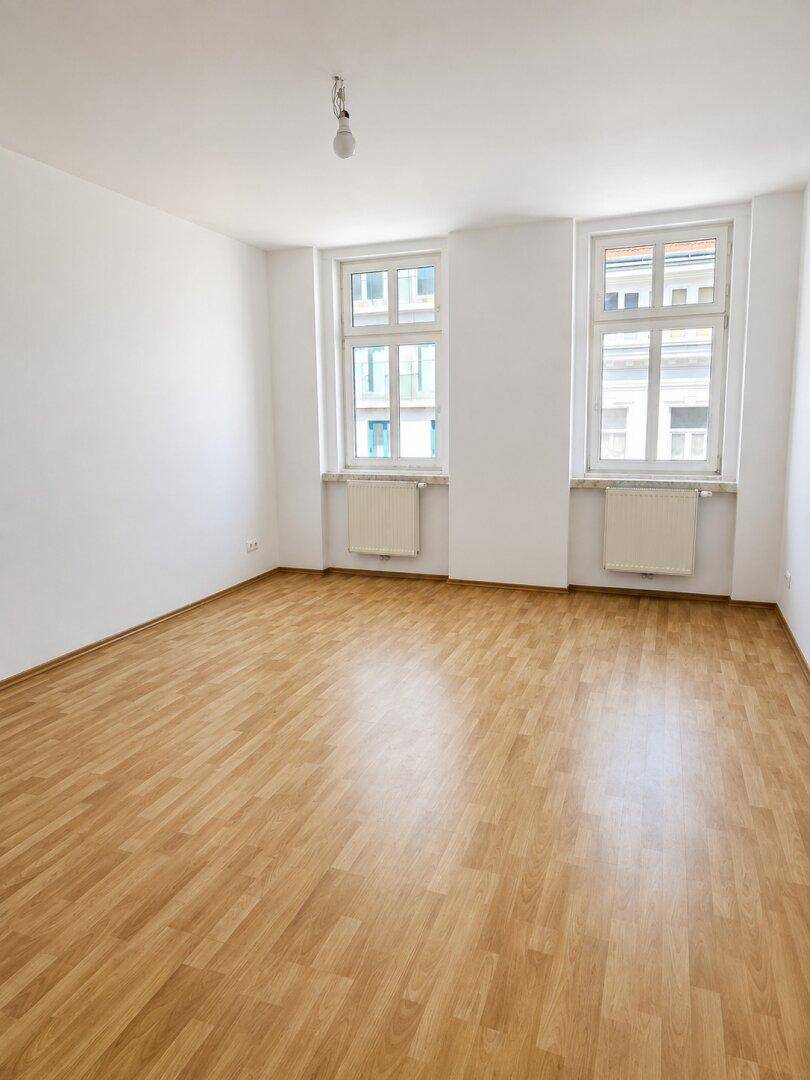 Geräumiges, helles Zimmer mit Laminatboden und zwei Fenstern, ideal für Wohn- oder Schlafbereich.