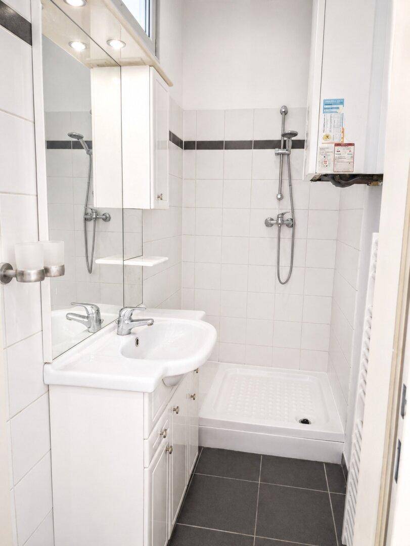 Kleines Badezimmer mit Dusche, Waschbecken und Spiegelschrank, ausgestattet mit weißen Fliesen.