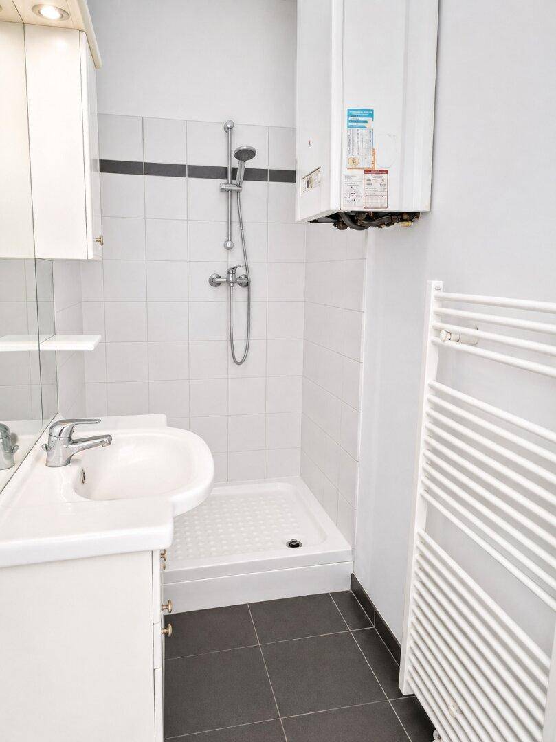 Funktionales Badezimmer mit Duschkabine, Waschbecken und Heizkörper, in hellen Fliesen gehalten.