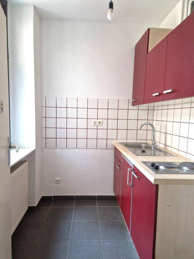 Kompakte Küchenzeile mit roten Schränken, Spüle und Kochfeld, ideal für kleine Wohnungen.