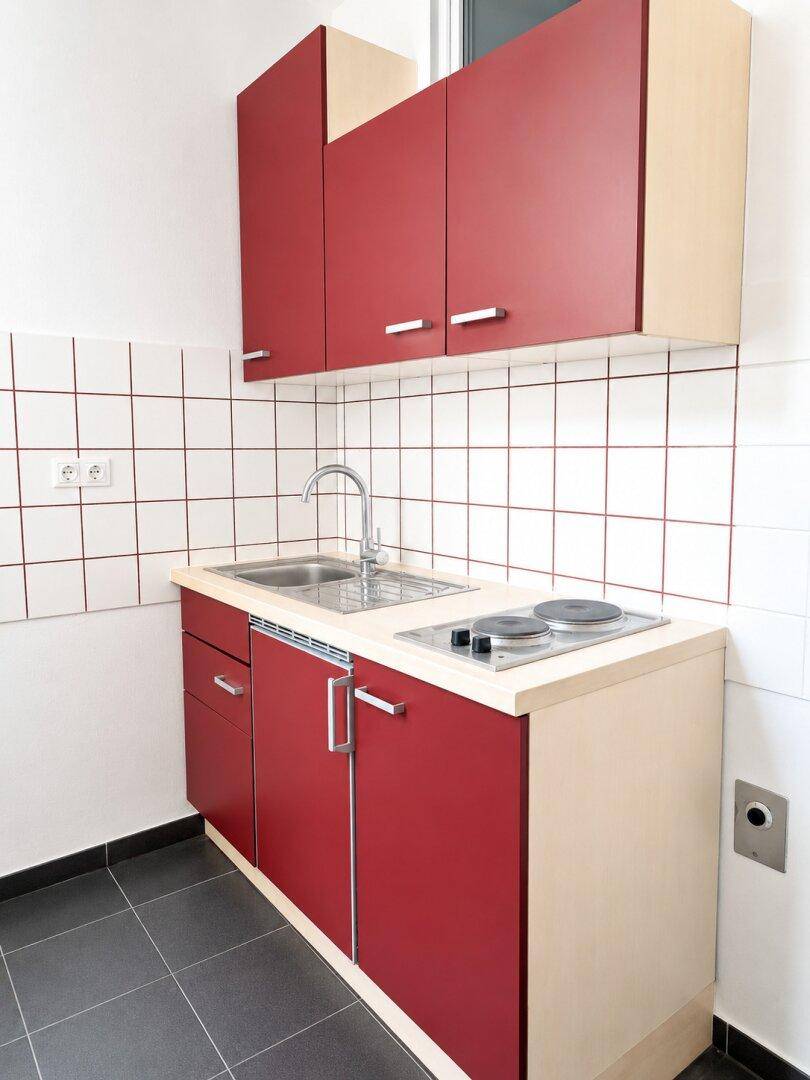 Moderne Küchenzeile mit roten Fronten, integriertem Kochfeld und Spüle, auf dunklem Fliesenboden.