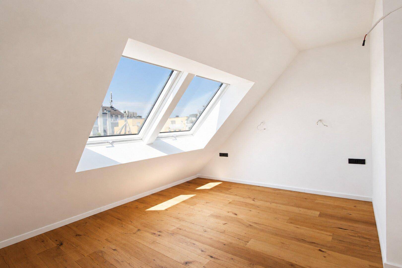 Lichtdurchfluteter Dachgeschossraum mit Holzboden und zwei großen Dachfenstern, bietet viel Tageslicht.