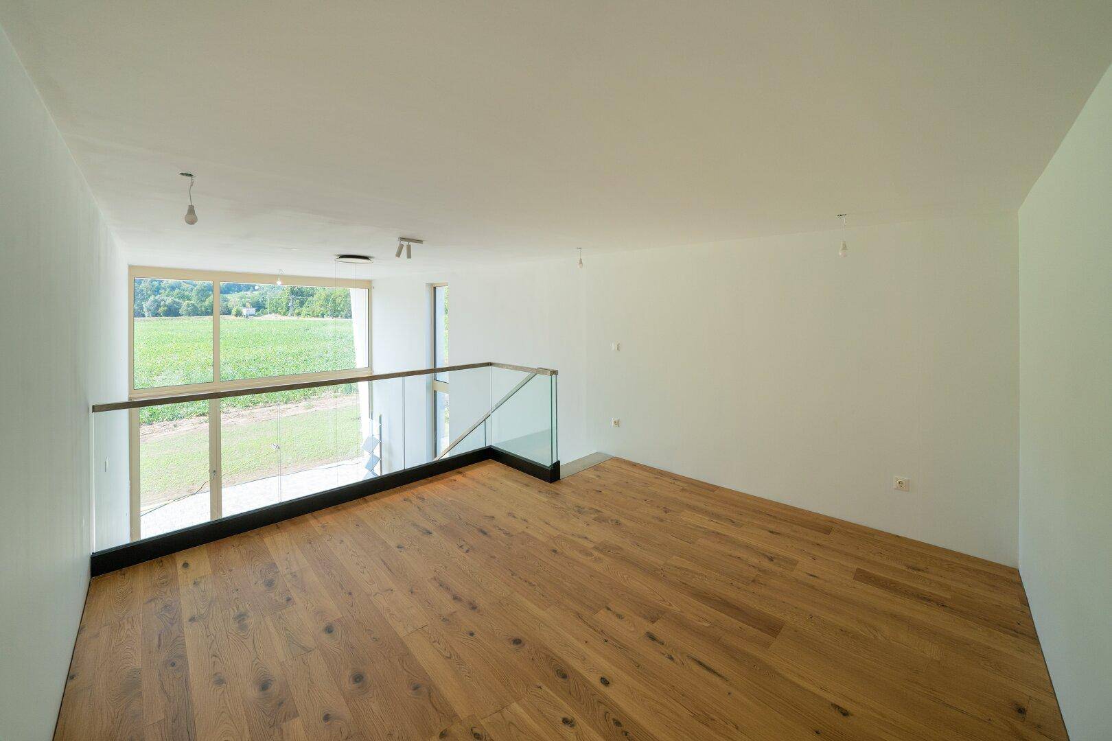 Heller offener Raum im Obergeschoss mit Holzboden und weitem Blick auf die Landschaft.