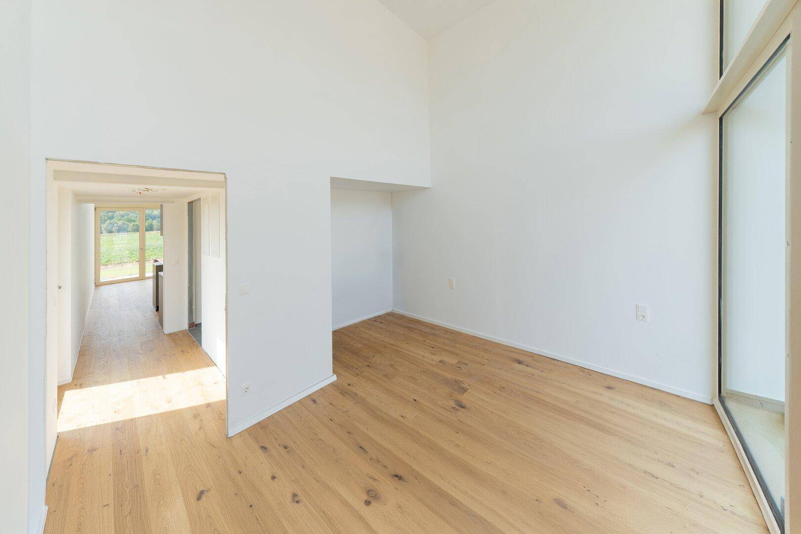 Heller, leerer Raum mit Holzboden, hohen Decken und Zugang zu einem weiteren Zimmer.